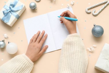 2025 yılını Noel baloları ve bej arka planda hediyeler içeren bir not defterine yazan kadın.