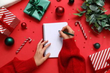 2025 yılını Noel dekoru ve kırmızı arka planda sunumlarla geçiren bir kadın.