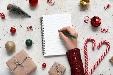 Noel süslemeleri ve hediye kutularıyla 2025 yıllık planları olan bir kadın grunge beyaz arka plan üzerine not defterine yazmış.