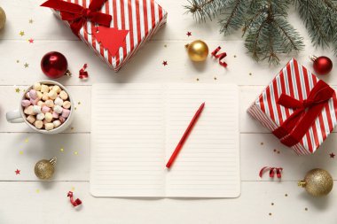 Noel süslemeleri, hediye kutuları ve beyaz ahşap arka planda bir fincan kakao olan defteri aç