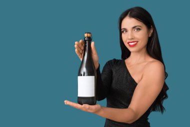 Mavi arka planda bir şişe şampanyası olan güzel, genç bir kadın.