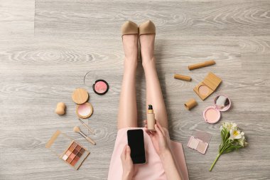 Cep telefonu ve kozmetik ürünleri ile ahşap zeminde makyaj sanatçısı, üst görünüm