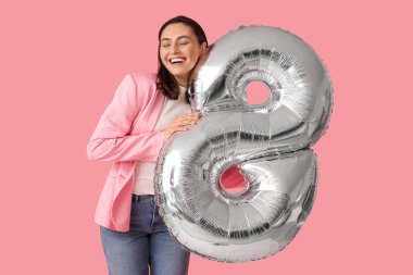 Pembe arka planda 8 şeklinde gümüş renkli balonu olan mutlu genç bir kadın. Uluslararası Kadınlar Günü