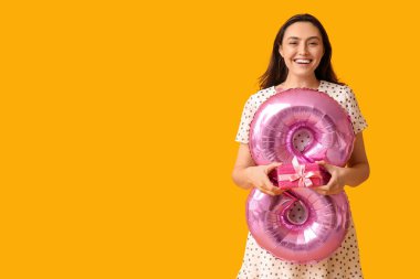 Pembe hava balonu olan güzel bir genç kadın. Şekil 8 ve sarı arka planda hediye kutusu. Uluslararası Kadınlar Günü