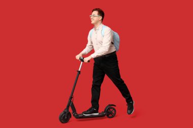 Kırmızı arka planda modern elektrikli scooter kullanan genç adam.
