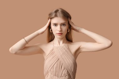 Kahverengi arka planda şık mücevherleri olan güzel genç bir kadın.