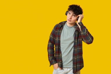 Sarı arka planda şık kıyafetler ve kulaklıklar takan yakışıklı bir genç.
