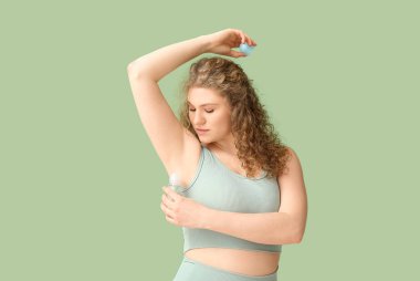 Yeşil arka plana deodorant süren güzel genç bir kadın.