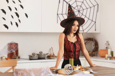 Cadılar Bayramı için cadı gibi giyinmiş güzel bir Asyalı kadın. Mutfakta süslemeleri var.