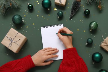 2025 yılını Noel dekoru ve yeşil arka planda hediyelerle geçiren bir kadın.