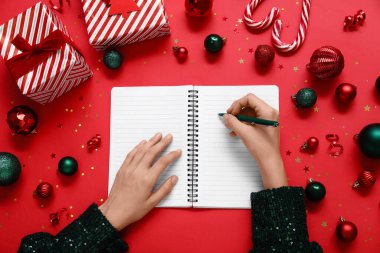 2025 yılını Noel dekoru ve kırmızı arka planda hediyelerle geçiren bir kadın.