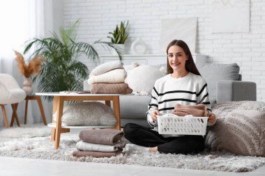 Evde kalın kazaklar katlayan genç bir kadın.