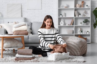 Evde kalın kazaklar katlayan genç bir kadın.