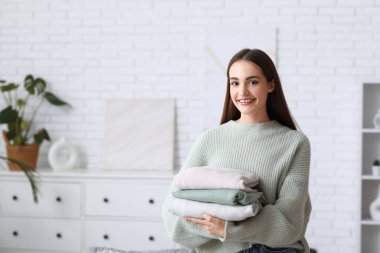 Evde bir yığın kalın kazağı olan genç bir kadın var.