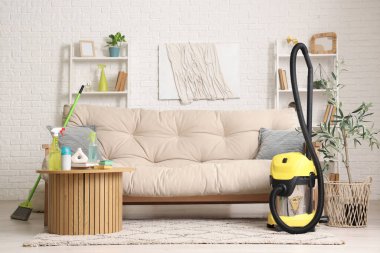 Oturma odasının içinde kanepe, masa ve temizlik malzemeleri var.