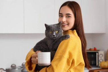 Sonbahar günü mutfakta bir fincan çay ve sevimli İngiliz kedisiyle genç bir kadın.