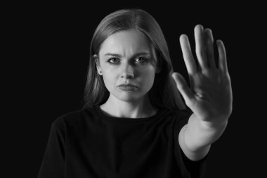 Ağlayan genç kadın siyah arka planda DUR hareketi gösteriyor