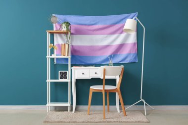 Masası, raf ünitesi ve transseksüel bayrağı olan odanın içi