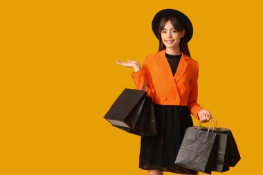 Alışveriş torbalı genç bir kadın sarı arka planda bir şey gösteriyor. Kara Cuma İndirimi