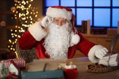 Noel Baba, Noel arifesinde evdeki masada mektuplarla oturuyor.