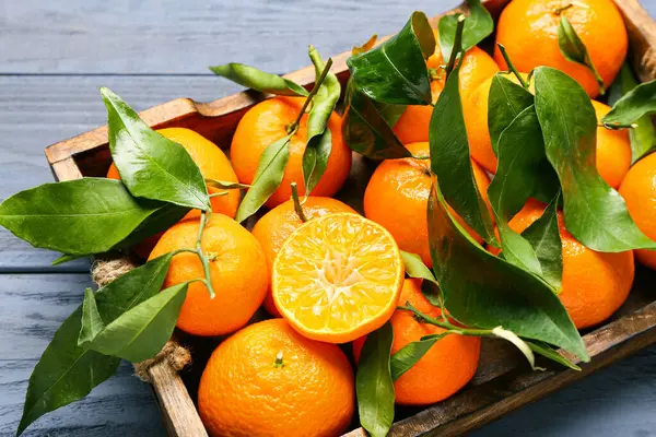 Tray with sweet mandarins and leaves on blue wooden background