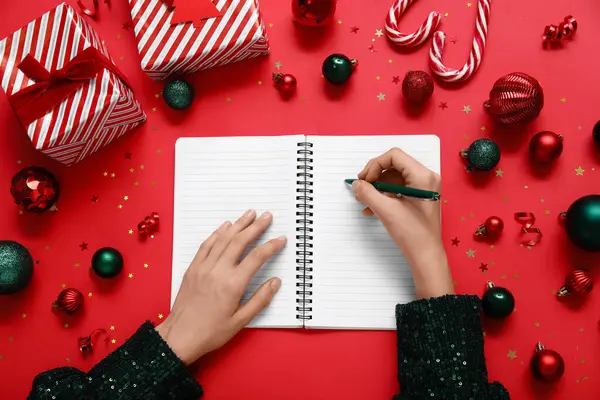 2025 yılını Noel dekoru ve kırmızı arka planda hediyelerle geçiren bir kadın.