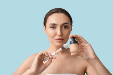 Makyaj temeli ve mavi arka planda fırçası olan genç kadın, yakın plan.