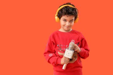 Kulaklıklı, turuncu arka planda mikrofonu olan sevimli bir çocuk.