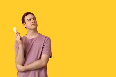 Sarı arka planda vibratörü olan düşünceli genç bir adam.