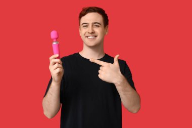 Kırmızı arka planda vibratöre bakan yakışıklı genç adam.