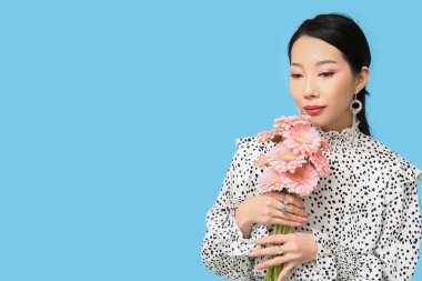 Mavi arka planda pembe Gerbera çiçekleri olan güzel bir Asyalı kadın.