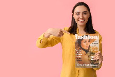 Güzel bir kadın pembe arka planda moda dergisini işaret ediyor.