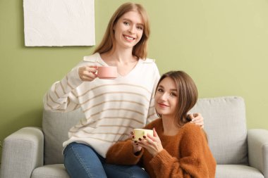 Evdeki kanepede çay içen genç kadınlar.