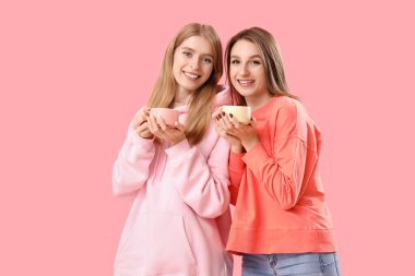 Pembe arka planda çay fincanları olan güzel genç kadınlar.