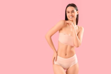 Pembe arka planda pamuklu iç çamaşırlı zayıf genç bir kadın.