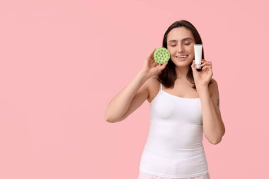 Saç derisi masaj aleti ve pembe arka planda kozmetik kremi olan güzel bir kadın.