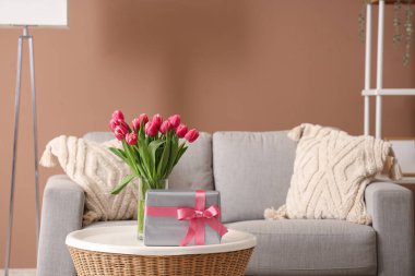 Çiçekli vazo ve hediye paketi oturma odasındaki sehpanın üzerinde.