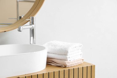 Banyodaki beyaz duvarın yanında lavabo ve temiz yumuşak havlu yığını.