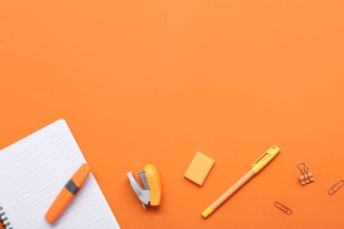 Turuncu arka planda kırtasiye malzemesi olan defter. Üst görünüm