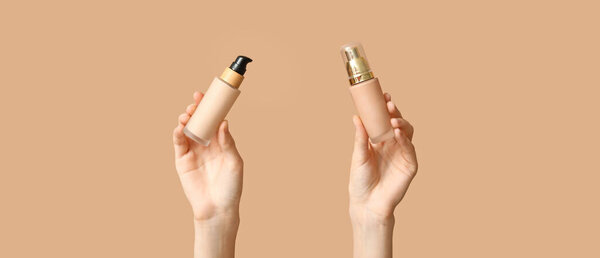 Female hands with bottles of makeup foundation on beige background