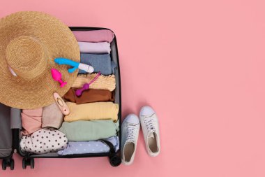 İçinde giysiler, hasır şapka, seks oyuncakları ve pembe arka planda ayakkabılar olan bavulu aç