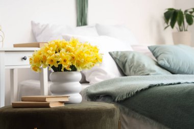 Nergisli vazo ve yatak odasında yeşil pouf üzerine kitaplar, yakın plan.