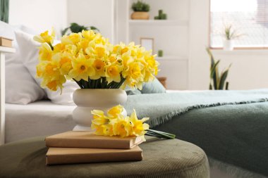 Nergisli vazo ve yatak odasında yeşil pouf üzerine kitaplar, yakın plan.