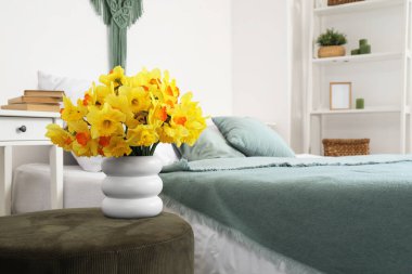 Üzerinde nergis olan vazo, yatak odasında yeşil pouf, yakın plan.