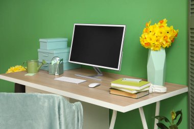 Ofiste yeşil duvarın yanında bilgisayar monitörlü ve nergisli modern işyeri