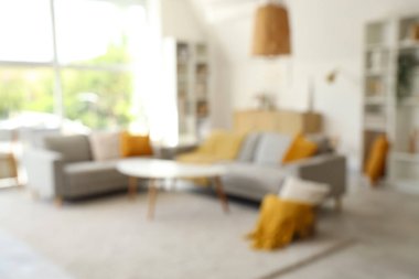 Gri kanepeler, masa ve raf üniteleriyle aydınlık oturma odasının bulanık görüntüsü