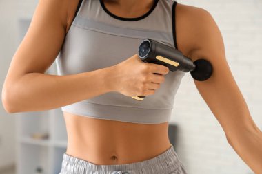 Spor salonundaki eğitimden sonra vurmalı masaj aleti kullanan genç bir kadın.