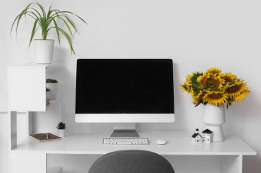 Bilgisayarlı modern çalışma alanı ve hafif ev ofisinde bir buket ayçiçeği.