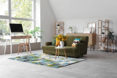 Oturma odasının içinde yeşil kanepe, modern çalışma alanı ve kahve masasında ayçiçekleri var.