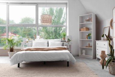 Beyaz çekmeceli, raf üniteli, ev bitkileri ve yataklı modern yatak odası.